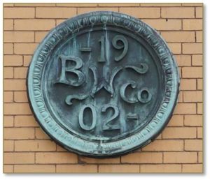 The Boston Wharf Company’s staff architects designed ranks of warehouses between the 1880s and the 1920s in uniform heights and sizes. The buildings are constructed of masonry with “classically inspired details concentrated at the entrances and cornices,” and flat roofs. A circular copper medallion stamps each of the buildings with a BWC logo in relief. 
